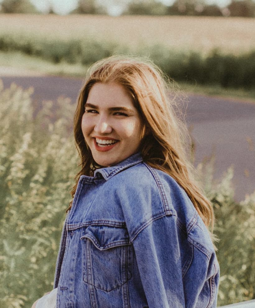 Emma, Designer and photographer smiling at the camera in a field.