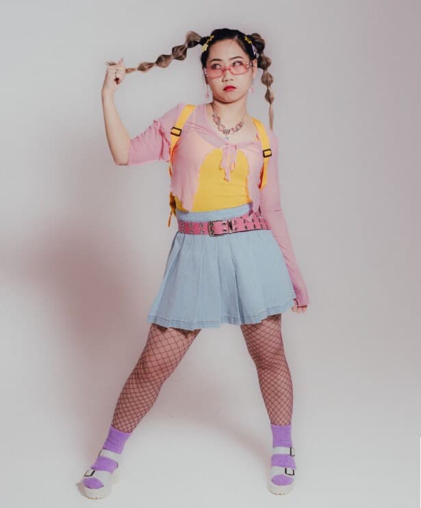 UX Lead, Michaela, posing with braided hair, wearing a pink, yellow, blue and purple K-POP dance crew outfit.